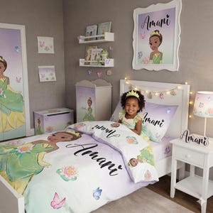 Puede incluir: Un juego de dormitorio con temática de princesa, que incluye una cama con ropa de cama, un cuadro enmarcado, una lámpara y una mesita de noche. La ropa de cama tiene el nombre "Amani" impreso. La combinación de colores incluye tonos de morado, verde y amarillo.