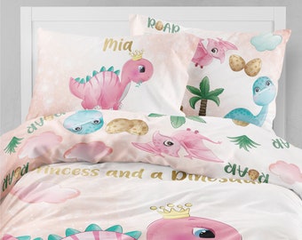 May include: A pink and white bedding set with a dinosaur theme. The bedding features a pink dinosaur with a crown, a blue dinosaur, and the words "princess and a dinosaur".