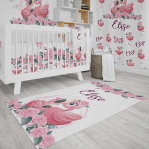 Puede incluir: Una cuna blanca con un juego de ropa de cama de estampado floral rosa y verde. La cuna está decorada con un flamenco rosa y el nombre "Elise" está escrito en la pared. Una alfombra floral rosa y verde con un diseño de flamenco está en el suelo.