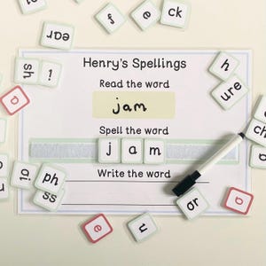 Może przedstawiać: Zielona i biała mata edukacyjna z napisem "Henry's Spellings" u góry. Mata ma sekcję do czytania, pisania i układania liter w słowo "jam". Wokół maty rozrzucone są literowe kafelki.
