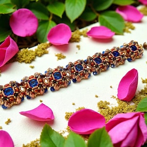 Puede incluir: Una pulsera de cuentas con un cierre dorado, con cuentas cuadradas azules y marrones. La pulsera está rodeada de pétalos de rosa rosas, hojas verdes y pequeños trozos de materia vegetal seca.