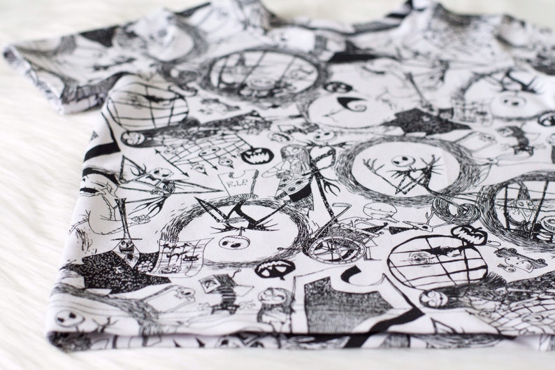 May include: Black and white t-shirt featuring a repeating pattern of characters from the film The Nightmare Before Christmas. The characters include Jack Skellington, Sally, and Oogie Boogie.