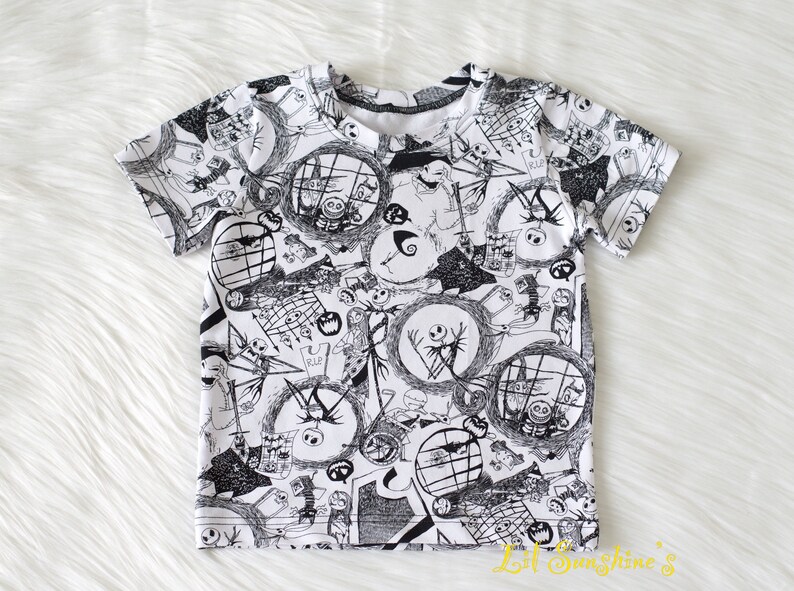 May include: A white t-shirt featuring a black and white print of characters from the film "The Nightmare Before Christmas".