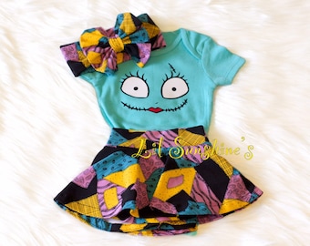 May include: A baby outfit set featuring a turquoise bodysuit with a Jack Skellington face, a black and turquoise patchwork skirt, and a matching headband with a large bow.
