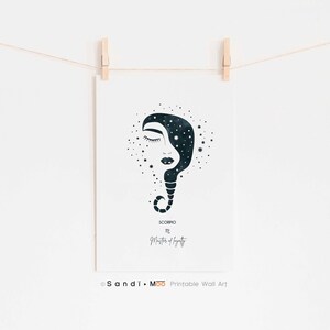Puede incluir: Una impresi&oacute;n blanca con una ilustraci&oacute;n azul oscuro de un rostro femenino y un dise&ntilde;o estrellado. La impresi&oacute;n est&aacute; etiquetada como "Scorpio" y "Masters of Intensity". La impresi&oacute;n est&aacute; colgada de una pinza de madera en una cuerda blanca.