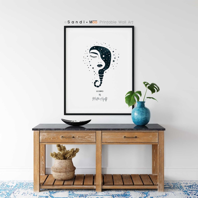 Puede incluir: Una impresi&oacute;n art&iacute;stica enmarcada con una ilustraci&oacute;n en azul oscuro y blanco de un rostro con dise&ntilde;o celestial, etiquetada como "Escorpio". La obra de arte se exhibe sobre una consola de madera con tapa negra, un jarr&oacute;n azul y un cuenco decorativo.