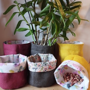 Peut inclure: Plusieurs pots de plantes en tissu de différentes couleurs, dont bordeaux, gris et jaune. Les pots ont des doublures à motifs floraux et contiennent des plantes et de petites perles en bois. Les pots sont en tissu texturé.