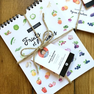 May include: A white calendar with a spiral binding featuring watercolor illustrations of fruits and vegetables. The calendar is titled "Fruits et L&eacute;gumes" and is tied with twine. A business card for Myriam Descl&egrave;ves, Illustratrice, is attached to the twine.
