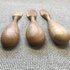 以下が含まれることがあります： 涙の形をしたボウルと丸みを帯びたハンドルが付いた3つの木製スクープ。スクープは明るい色の木材で作られており、滑らかな仕上がりです。それらは、テクスチャ加工されたニュートラルカラーの表面に配置されています。