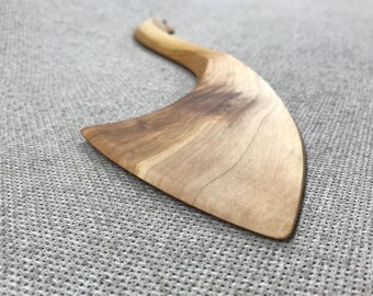 May include: A wooden butter knife with a curved handle and a wide, flat blade. The knife is made of light brown wood with a natural grain pattern.