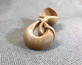 May include: A light-colored wooden spoon featuring a smooth, polished finish and a unique, intricately carved handle that loops back on itself. The bowl of the spoon is rounded and shallow, showcasing the natural grain and texture of the wood.