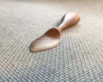 May include: A small, wooden spoon with a rounded, spoon-like end and a long, thin handle. The spoon is made of light-colored wood and has a smooth, polished finish.