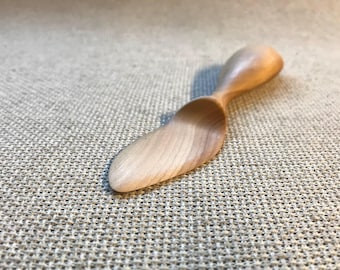 May include: A wooden butter knife with a unique, twisted handle. The knife is made of light-colored wood and has a smooth, polished finish.