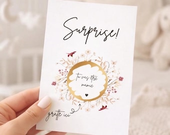 Peut inclure: Une carte rectangulaire blanche avec le texte noir Surprise! en haut, une zone à gratter circulaire dorée au centre entourée d'une couronne florale délicate dans des tons rose et bordeaux, et le texte noir gratte ici avec une flèche.