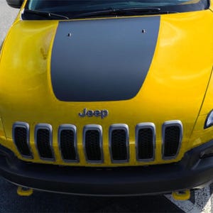 以下が含まれることがあります： 黒いボンネットとフロントバンパーを備えた明るい黄色のジープチェロキー。ジープのロゴがフロントグリル上に見えます。フロントグリルには7つの垂直スロットがあります。