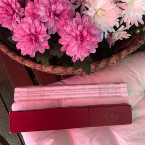 May include: A vintage slide rule in a red case. The slide rule is white with black markings. The case has a gold circle with a letter P in the center.