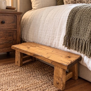 May include: A low rectangular wooden bench with a natural light brown finish and visible wood grain. The bench features four sturdy block legs and a thick, flat top surface, constructed from solid timber with a rustic, unpainted appearance.