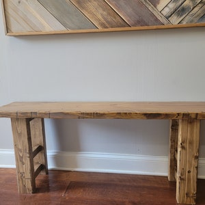 May include: A rustic wooden bench with a natural wood finish. The bench has a wide, flat top and two sturdy legs. The bench is made of reclaimed wood and has a unique, handcrafted look.
