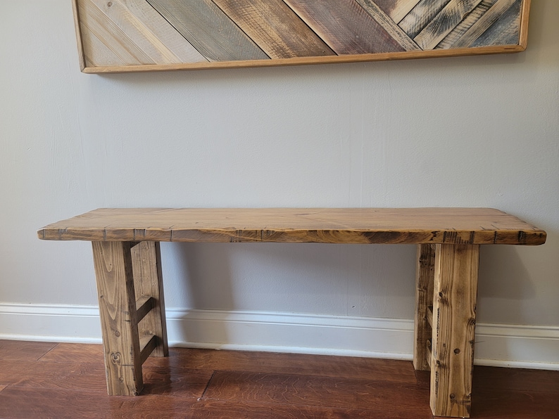 May include: A rustic wooden bench with a natural wood finish. The bench has a wide, flat top and two sturdy legs. The bench is made of reclaimed wood and has a unique, handcrafted look.