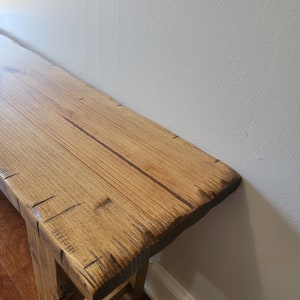 May include: A rustic wooden bench with a natural wood finish. The bench has a simple design with a wide, flat top and two legs. The wood has a natural grain pattern and is slightly distressed.