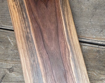 May include: A large, rectangular cutting board made of dark brown walnut wood. The wood grain is visible and has a natural, rustic look.
