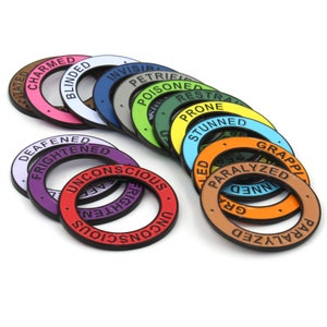 May include: A collection of colorful, circular game tokens with various status effect labels such as "Charmed," "Blinded," and "Paralyzed." Each token has a different color, including pink, blue, green, and orange, with white lettering.