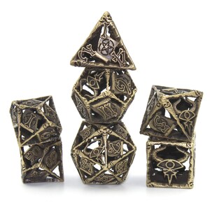 May include: A set of six gold metal dice with intricate designs, including skulls, bones, and eyes. The dice are stacked in a tower formation.