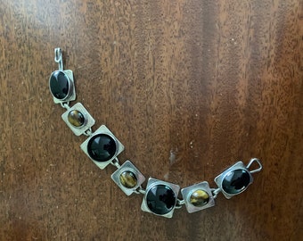 May include: A silver bracelet with alternating black and brown oval stones set in square frames.