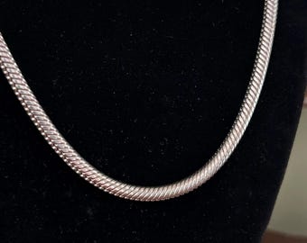 May include: A silver snake chain necklace on a black velvet background.