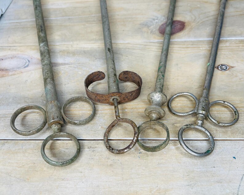 Peut inclure: Quatre outils anciens en m&eacute;tal avec de longs manches et des poign&eacute;es en forme d'anneau. Les outils ont une apparence vieillie et us&eacute;e avec des signes de rouille. Les manches sont cylindriques et les poign&eacute;es sont circulaires. Les outils sont dispos&eacute;s sur une surface en bois clair.