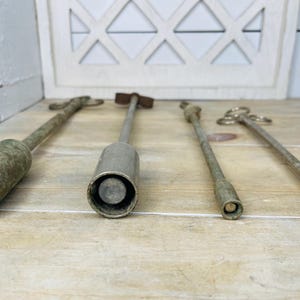 Peut inclure: Quatre outils anciens en m&eacute;tal de formes cylindriques et allong&eacute;es. Les outils ont un aspect vieilli et patin&eacute; avec des tons argent&eacute;s et bronze. Les outils sont dispos&eacute;s sur une surface en bois de couleur claire.