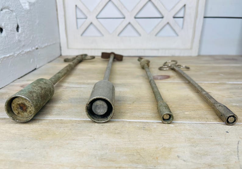 Peut inclure: Quatre outils anciens en m&eacute;tal de formes cylindriques et allong&eacute;es. Les outils ont un aspect vieilli et patin&eacute; avec des tons argent&eacute;s et bronze. Les outils sont dispos&eacute;s sur une surface en bois de couleur claire.