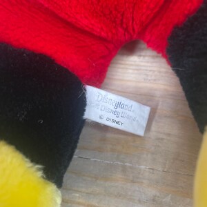 May include: A black, yellow and red plush toy with a white tag that reads "Disneyland and Walt Disney World" and "&copy; DISNEY".
