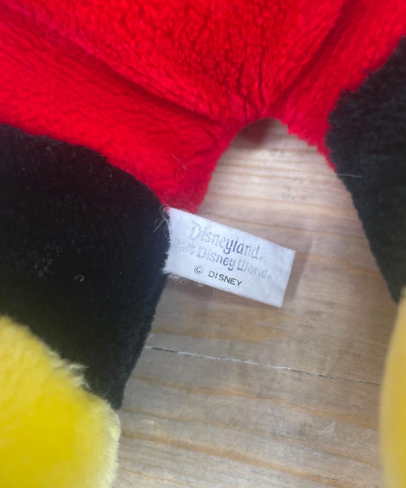May include: A black, yellow and red plush toy with a white tag that reads "Disneyland and Walt Disney World" and "&copy; DISNEY".