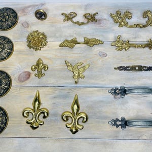 May include: Assortment of decorative hardware in gold and silver finishes.  Includes ornate pulls, knobs, and drawer pulls with floral and scroll designs.