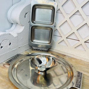 May include: Two-sectioned rectangular serving dish and a round serving tray with a small bowl, all in brushed silver. The rectangular dish has decorative handles and two square compartments. The round tray also has decorative handles.