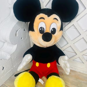 May include: A plush Mickey Mouse toy with black fur, large ears, yellow shoes, and a red and black outfit.