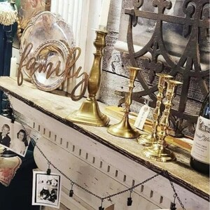 May include: A white shelf with a wooden top, decorated with vintage items, including a silver platter, candlesticks, and a metal anchor. The shelf is adorned with a wooden sign that reads "family".