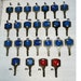 May include: Collection of 25 vintage keys with numbered circular inserts. Most inserts are blue, one is red. Keys are arranged in rows on a white surface. Numbers on key tags include: N, 146, 158, 212, 206, 112, 302, 37, 98, 742, 1001, 1110, 0157, 1210, 1213, 2114, 2142, 2154, 2098, 2122, 8672, 2216, 1222, 841, 375.