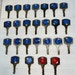 May include: Thirty vintage keys with blue and red circular number tags. The numbers on the tags are visible and range from single digits to four digits. The keys are metallic with a slightly aged appearance. The key tags are predominantly blue, with a few red ones. The keys are arranged in neat rows on a light-colored surface.