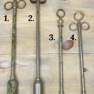 Peut inclure: Quatre outils anciens en m&eacute;tal de conceptions vari&eacute;es. Les outils ont de longues tiges minces et des sommets d&eacute;coratifs, notamment des anneaux et une poign&eacute;e incurv&eacute;e. Le m&eacute;tal a un aspect vieilli et patin&eacute;, certains pr&eacute;sentant des signes d'oxydation. Ils sont dispos&eacute;s sur une surface en bois.