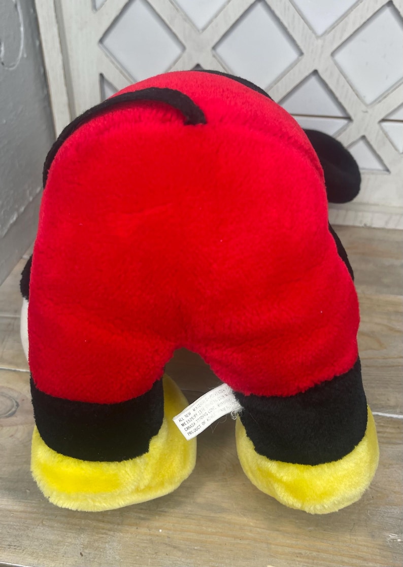 May include: Red, black and yellow plush toy of a cartoon dog. The toy has a tag on the bottom that reads "All New Material. Made in China. Reg. No. PA-11543 (CN) CA24145-17000. Product of China."