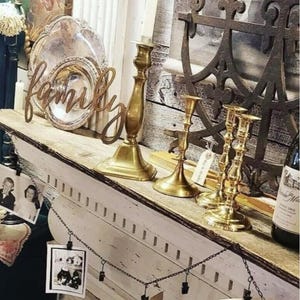 May include: A white shelf with a wooden top, decorated with vintage items, including a silver platter, candlesticks, and a metal anchor. The shelf is adorned with a wooden sign that reads "family".