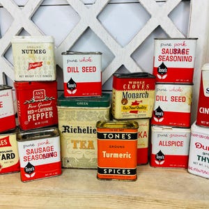 May include: A collection of vintage spice tins in various shapes and sizes. The tins feature labels with text such as "Nutmeg", "Sage", "Mustard", "Cinnamon", and "Thyme". The color palette includes red, white, yellow, and green.