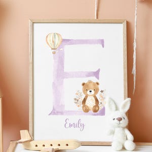 May include: A purple watercolor letter E with a brown bear and a hot air balloon. The name Emily is written below the letter.