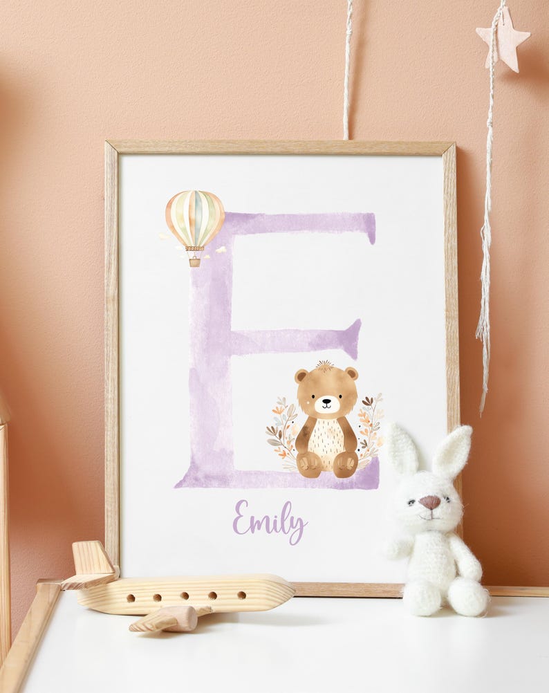 May include: A purple watercolor letter E with a brown bear and a hot air balloon. The name Emily is written below the letter.