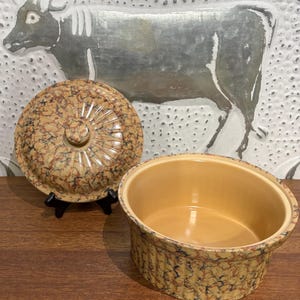 Può includere: Una casseruola in ceramica marrone e beige con coperchio. La casseruola ha un motivo marmoreo e un bordo rialzato. Il coperchio ha un pomo in cima.