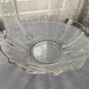May include: A clear glass serving bowl with a scalloped edge and two handles. The bowl has a delicate etched floral design.