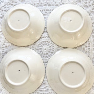 May include: Four white ceramic bowls with a scalloped edge. The bowls are turned upside down and have a small mark on the bottom.