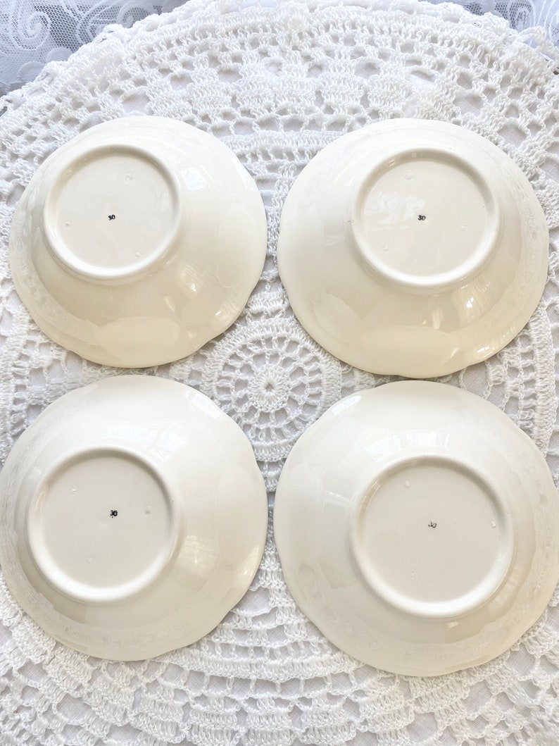 May include: Four white ceramic bowls with a scalloped edge. The bowls are turned upside down and have a small mark on the bottom.